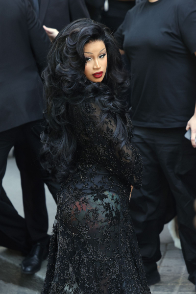 Cardi B attends a fashion show in a sheer beaded black dress red lipstick and full curls.
